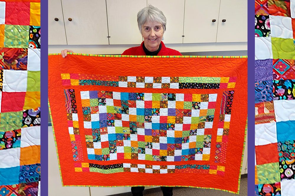 Donor Janet Clarke holds up Mystery Quilt.